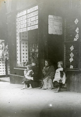 Three children and an elderly woman sitting outside a butcher's shop